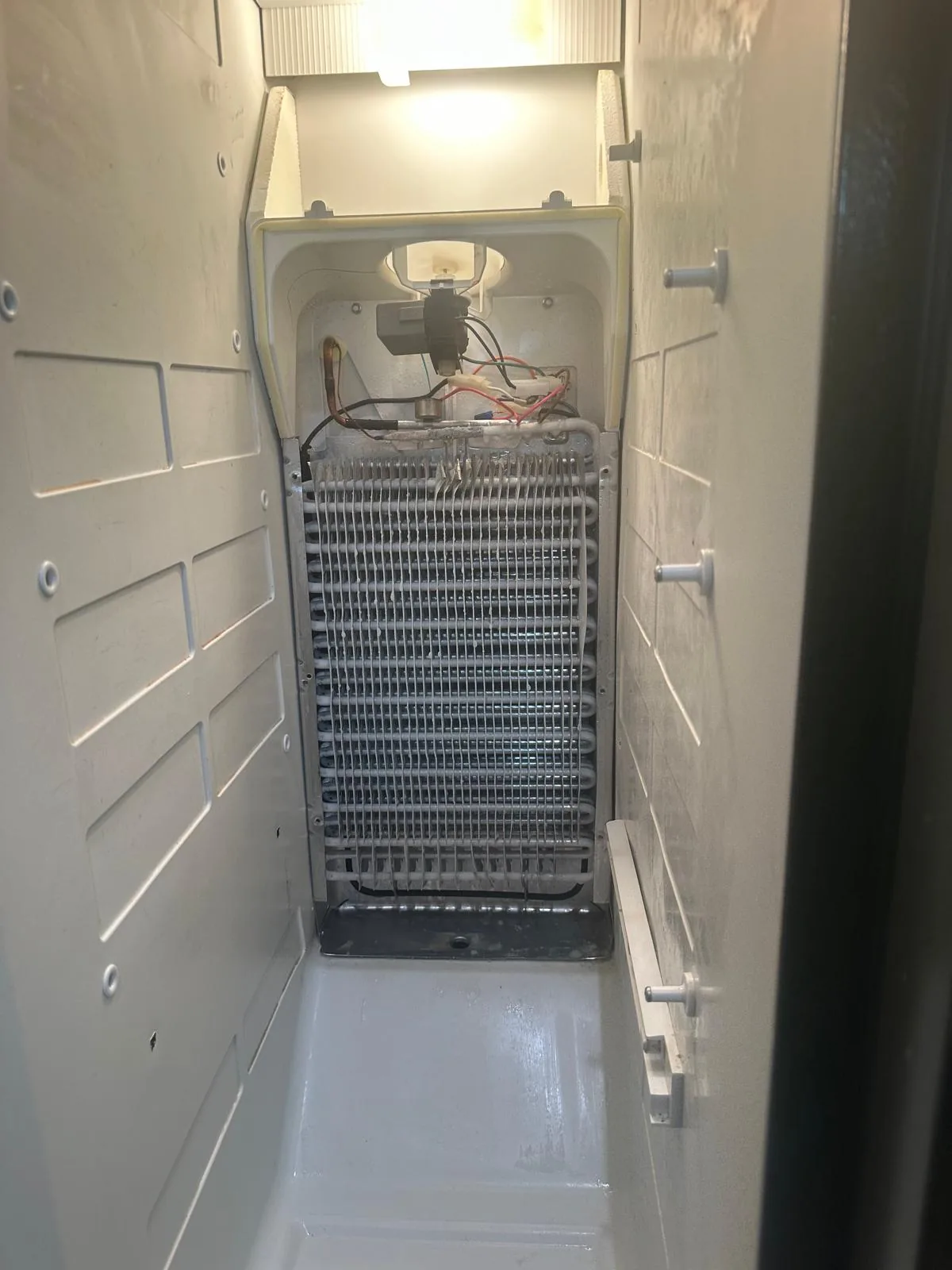 GE refrigerator freezer compartment opened with evaporator coils exposed for fan motor diagnosis